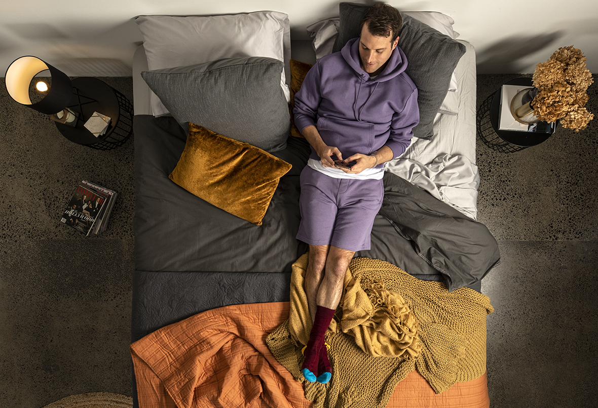 guy in purple outfit lying on a bed using his phone